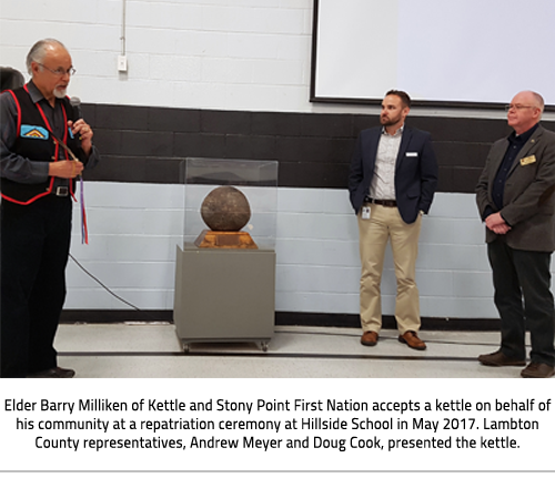 (Image Caption: "Elder Barry Milliken of Kettle and Stony Point First Nation accepts a kettle on behalf of his community at a repatriation ceremony at Hillside School in May 2017. Lambton County representatives, Andrew Meyer and Doug Cook, presented the kettle."), link.