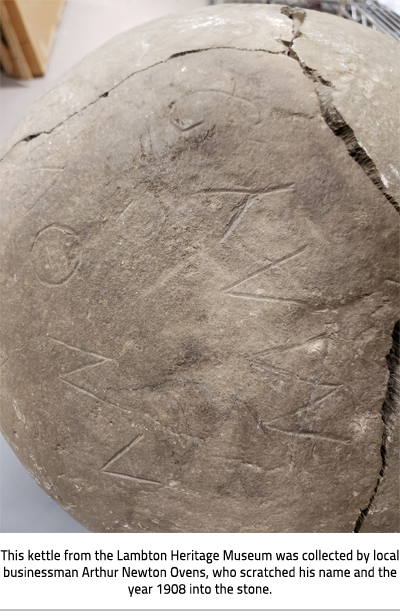 Large stone sphere with  etched letters and a big crack. Image Caption: "This kettle from Lambton Heritage Museum was collected by local businessman Arthur Newton Ovens, who scratched his name".), link.