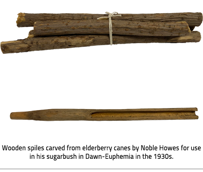 (At the top there is a bundle of wooden spiles. At the bottom is a single wooden spile. The left side is narrowed and rounded, a opening runs from the middle to the right end. Image Caption: "Wooden spiles carved from elderberry canes by Noble Howes for use in his sugarbush in Dawn-Euphemia in the 1930s."), link.