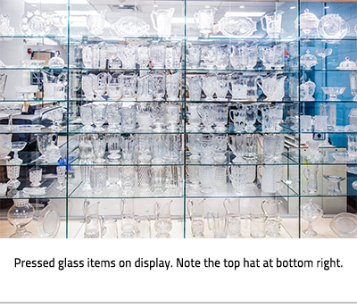 Pressed glass in a display case. Image Caption: "Pressed glass items on display. Note the top hat at the bottom right.", link.