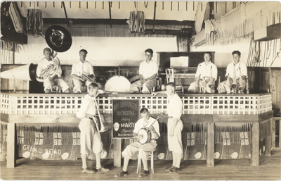 (A band is on and in front of a stage. The men on the stage have various instruments including a tuba. The men in front watch a man playing a banjo. The small banner on the middle of the stage reads: "Don Barringer's Orchestra"  the other text is partly obscured. on the left side of the postcard, the words "GRAND BEND" is etched.), link.