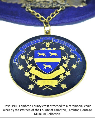 Large, circular, gold and dark blue pendant on a gold chain with the new Lambton Crest upon it. Image Caption: "Post- 1908 Lambton County crest attached to a ceremonial chain worn by the Warden of the County of Lambton, Lambton Heritage Museum Collection."), link