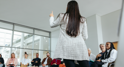 Female speaker leading a motivational seminar with a diverse group of attendees in a modern conference room.
