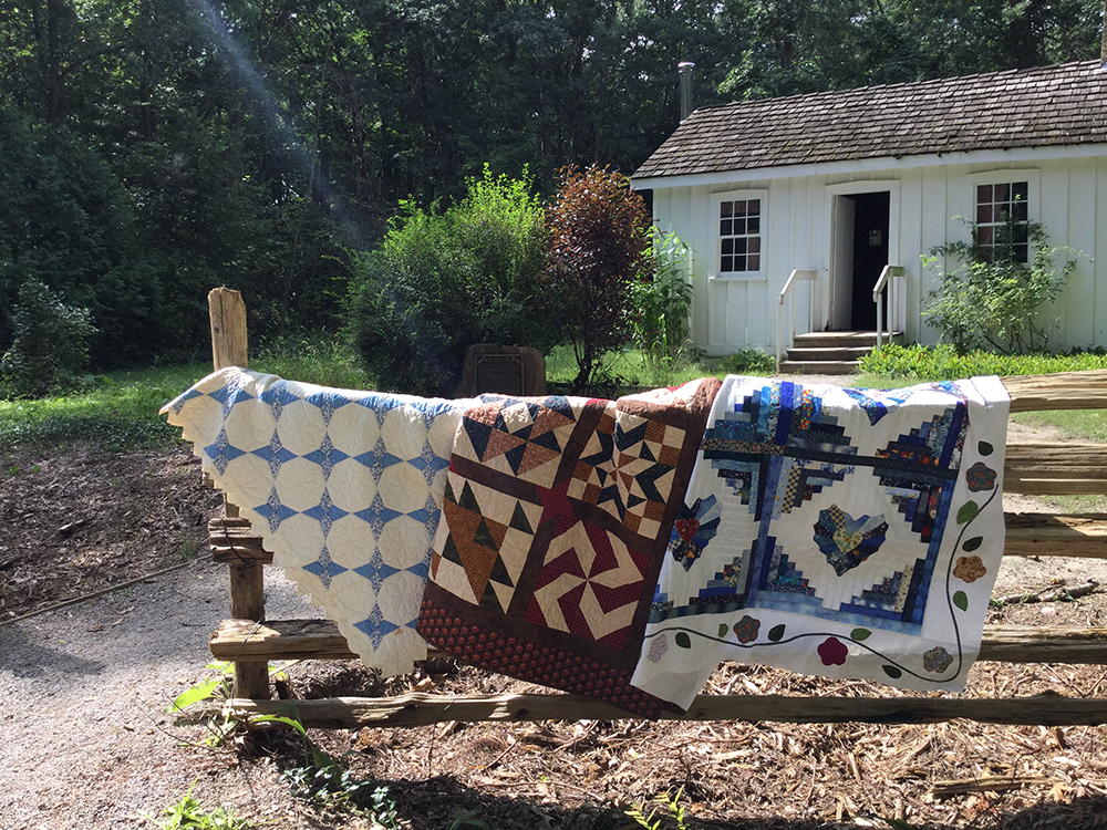 Quilts on display in front of the historic Tudhop House at Lambton Heritage Museum.