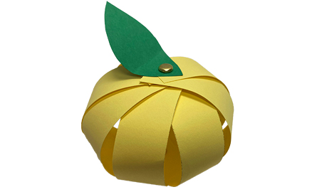 A yellow paper apple with a green paper leaf fastened to the top.