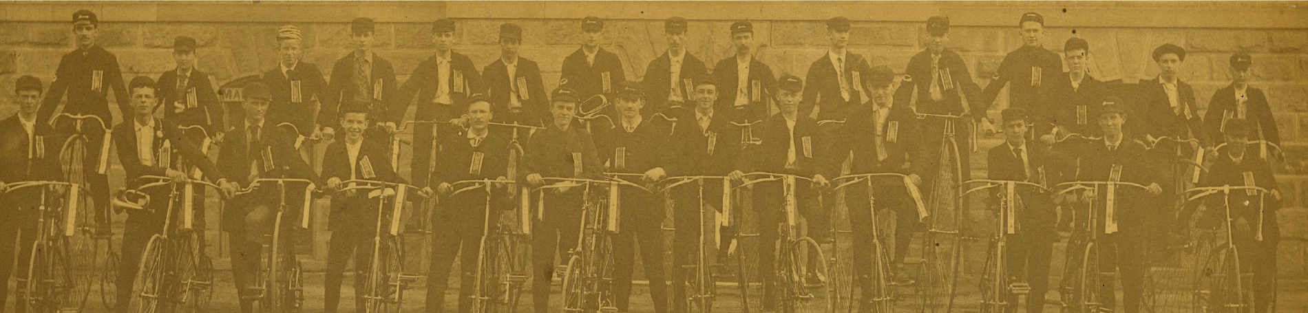Old photo of two rows of men standing next to bikes.
