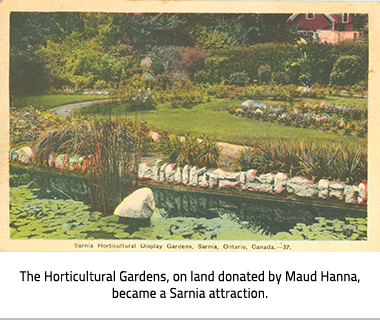 (Lush green gardens with pastel flowers, a pond at the front and a path through it. In the background there is a red brick house. Image Caption: "The Horticultural Gardens, on land donated by Maude Hanna."), link.