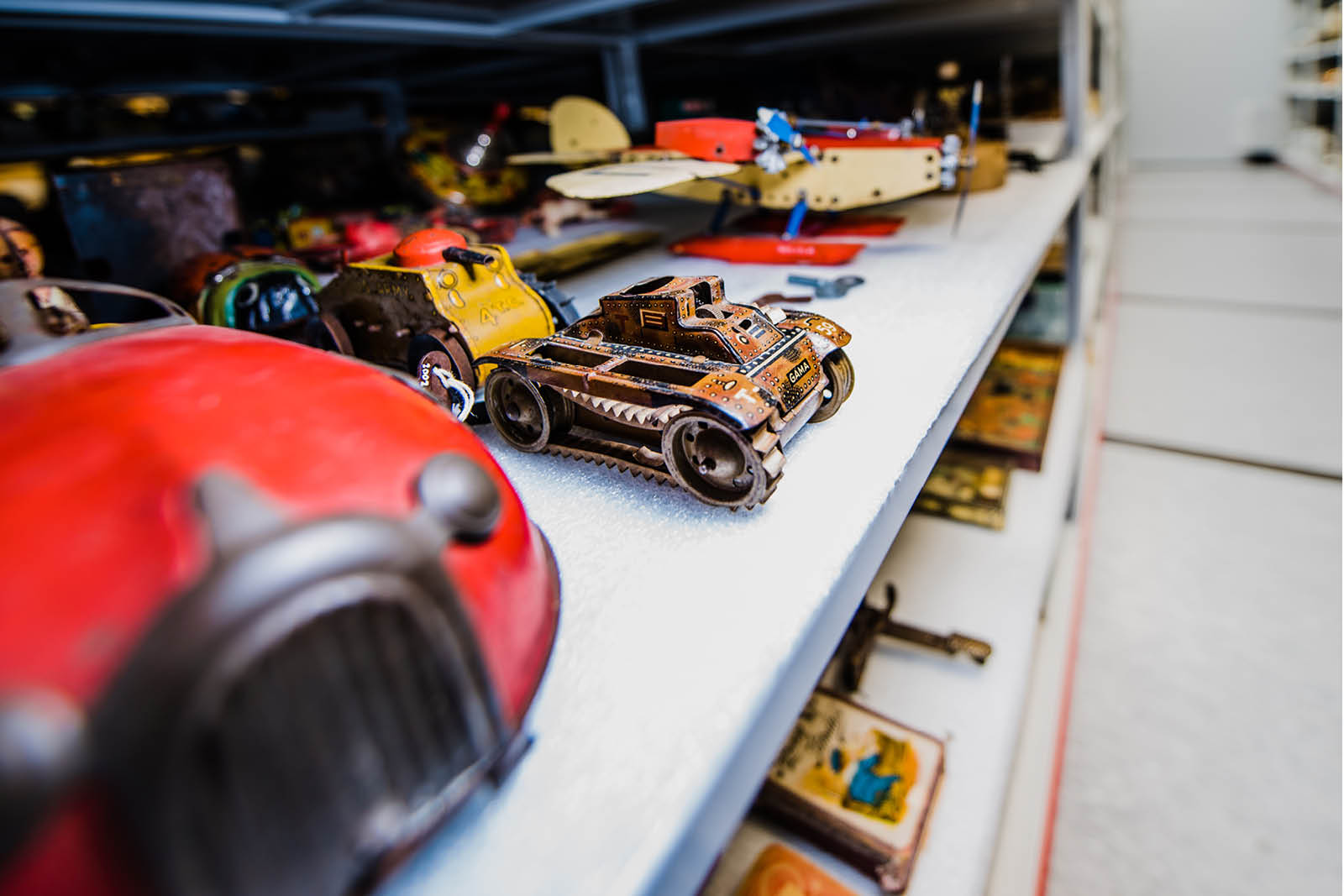 A metal toy car sits next to two metal toy tanks and a toy airplane on a metal shelf in Lambton Heritage Museum's collections centre.