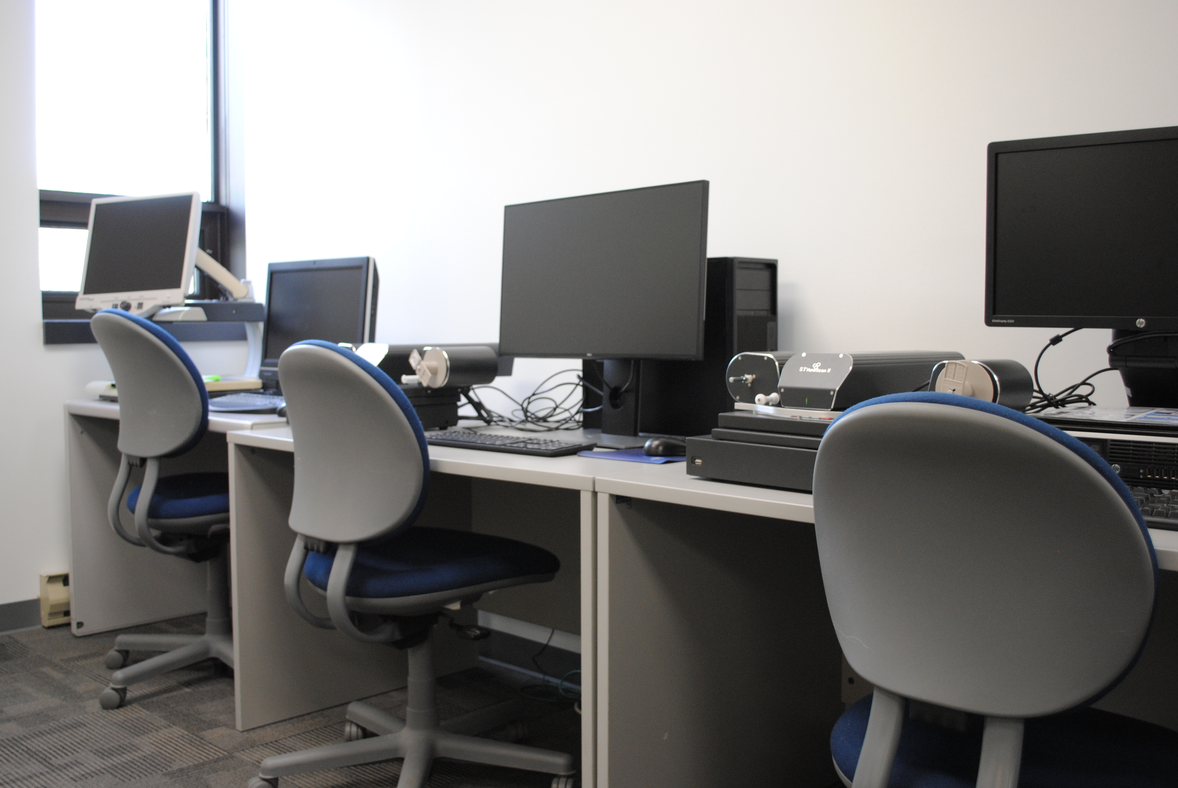 Computers on a desk with chairs in front of them.