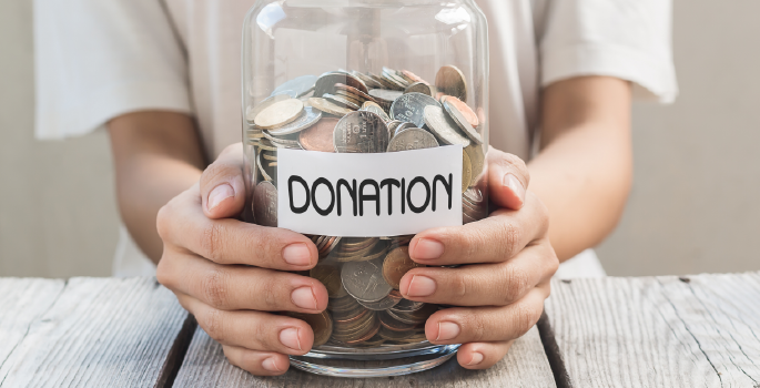 Hands holding a jar with words "donation" on it.