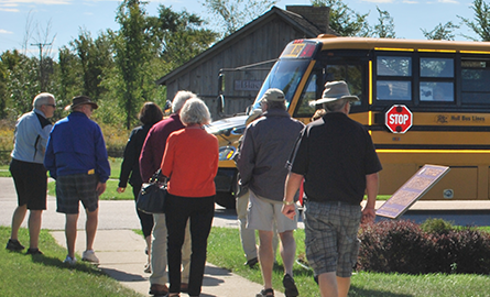 Groups of adults on museum grounds with a school bus in the background.