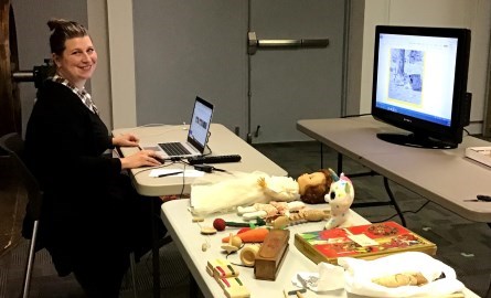 Lady sitting at table with laptop and artifacts.